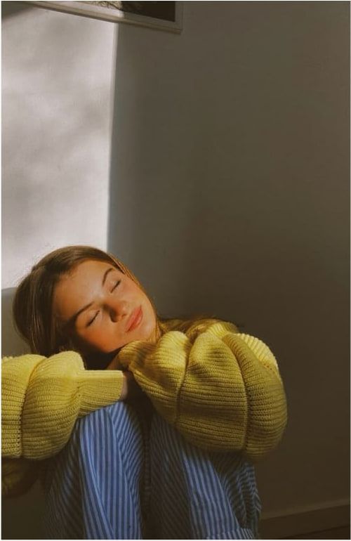 A woman leaning on a wall, eyes closed, in natural light